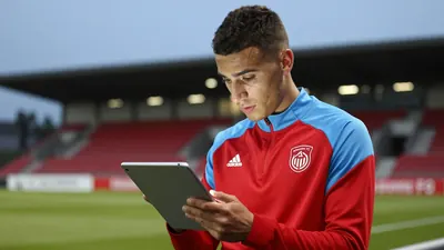 Waist-up shot of a focused, 28-year-old Annecy FC midfielder, clad in a plain, unmarked, red and sky blue training top...