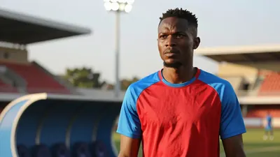 A medium shot of a Ghanaian full-back in his late 20s, wearing a plain red and sky blue crew-necked training top made of...