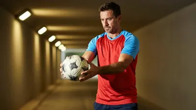 A 35-year-old, 5'10" athletic coach with a strong build, wearing a plain red and sky blue jersey made of lightweight...